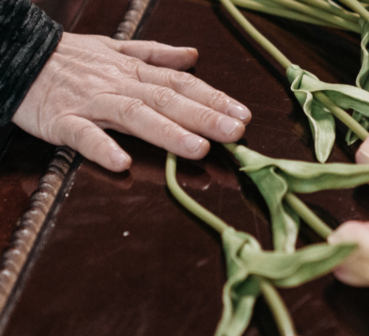 En hand rör vid stjälkarna av vissna blommor på en mörk yta.