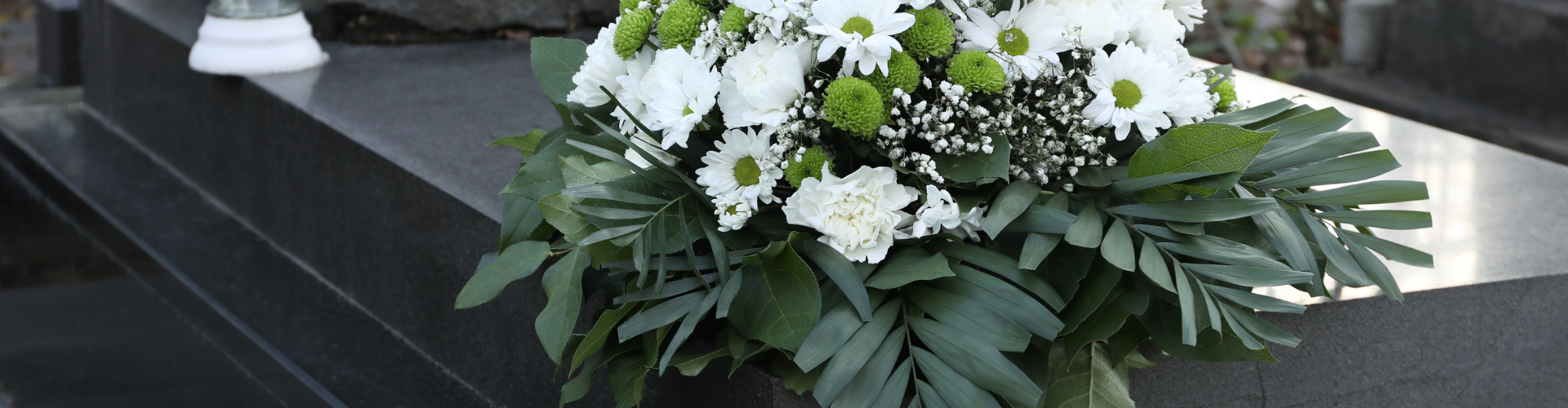 En bukett med vita blommor och gröna blad ligger på en mörk yta.