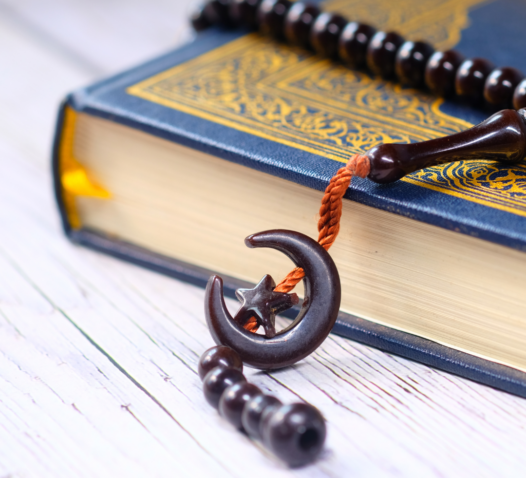 En bok med gulddetaljer ligger på ett bord med ett radband och en måneformad dekoration.