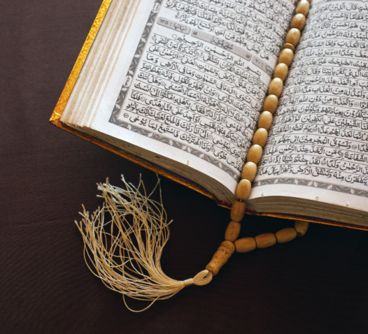 En uppslagen bok med en guldfärgad pärm visas tillsammans med ett radband och en tofs.