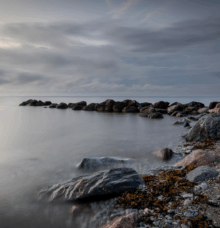 Kustlandskap med klippor och en lugn, molnig himmel.