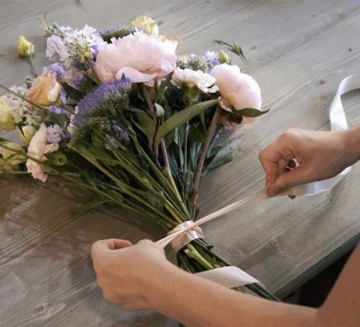 Händer knyter ett band runt en bukett med blommor på ett träbord.