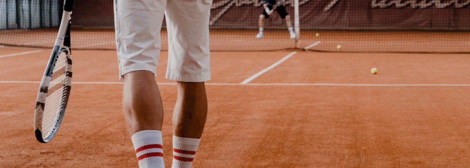En person spelar tennis på en grusbana.