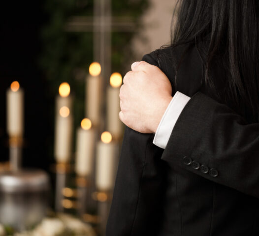 En person klädd i svart kostym håller om en annan person framför tända ljus.