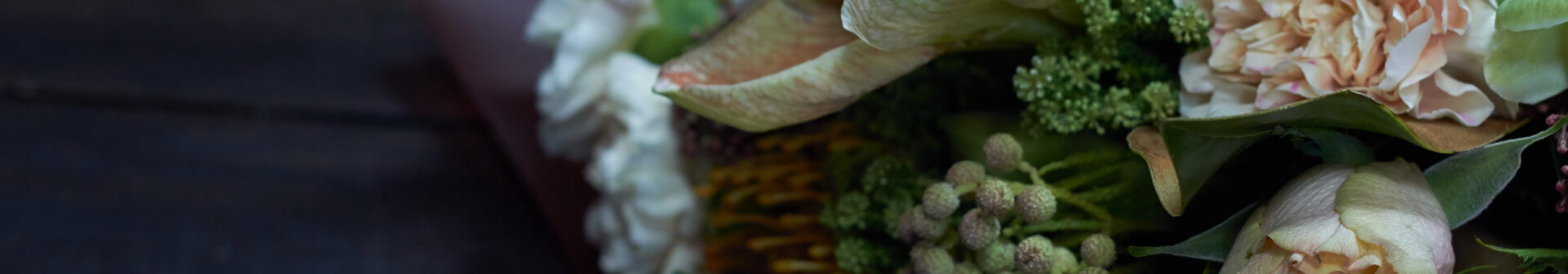 En bukett med olika blommor, inklusive rosor och bär, ligger på ett mörkt bord.