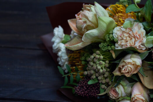 En bukett med olika blommor, inklusive rosor och bär, ligger på ett mörkt bord.