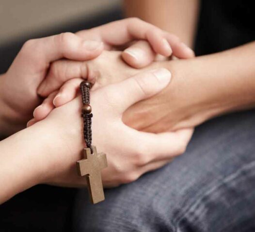 Händer som håller varandra, med ett träkors i bakgrunden.