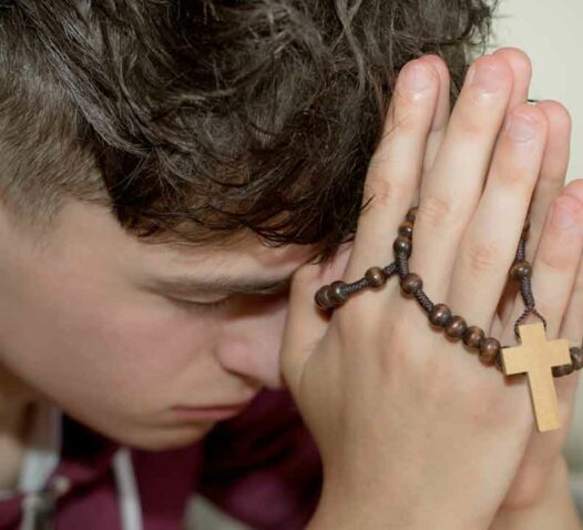 Person med slutna ögon håller händerna i bön med ett radband.