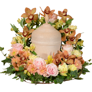 En urna omgiven av en krans av blommor i olika nyanser av rosa, gult och orange, inklusive rosor och orkidéer, med gröna blad som dekoration.